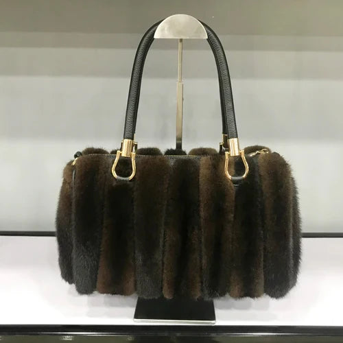 Brown fur handbag with gold accents on a stand against a white background