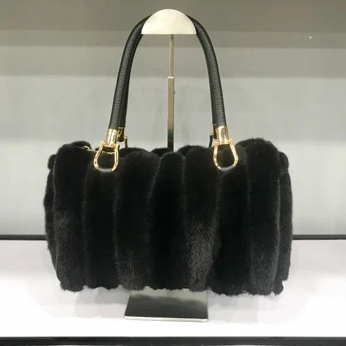 Black fur handbag with gold hardware on a stand against a neutral background