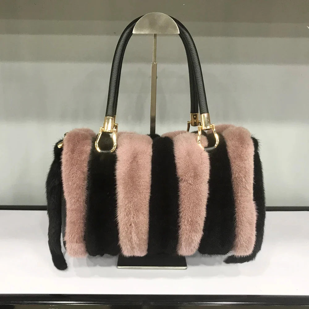 Black and pink striped handbag with gold accents on a stand against a neutral background