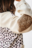 Close-up of a person wearing a beige quilted jacket with a leopard print garment underneath.