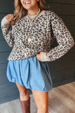 Woman in beige and brown leopard print knit sweater with blue denim skirt and brown boots against wood paneling.