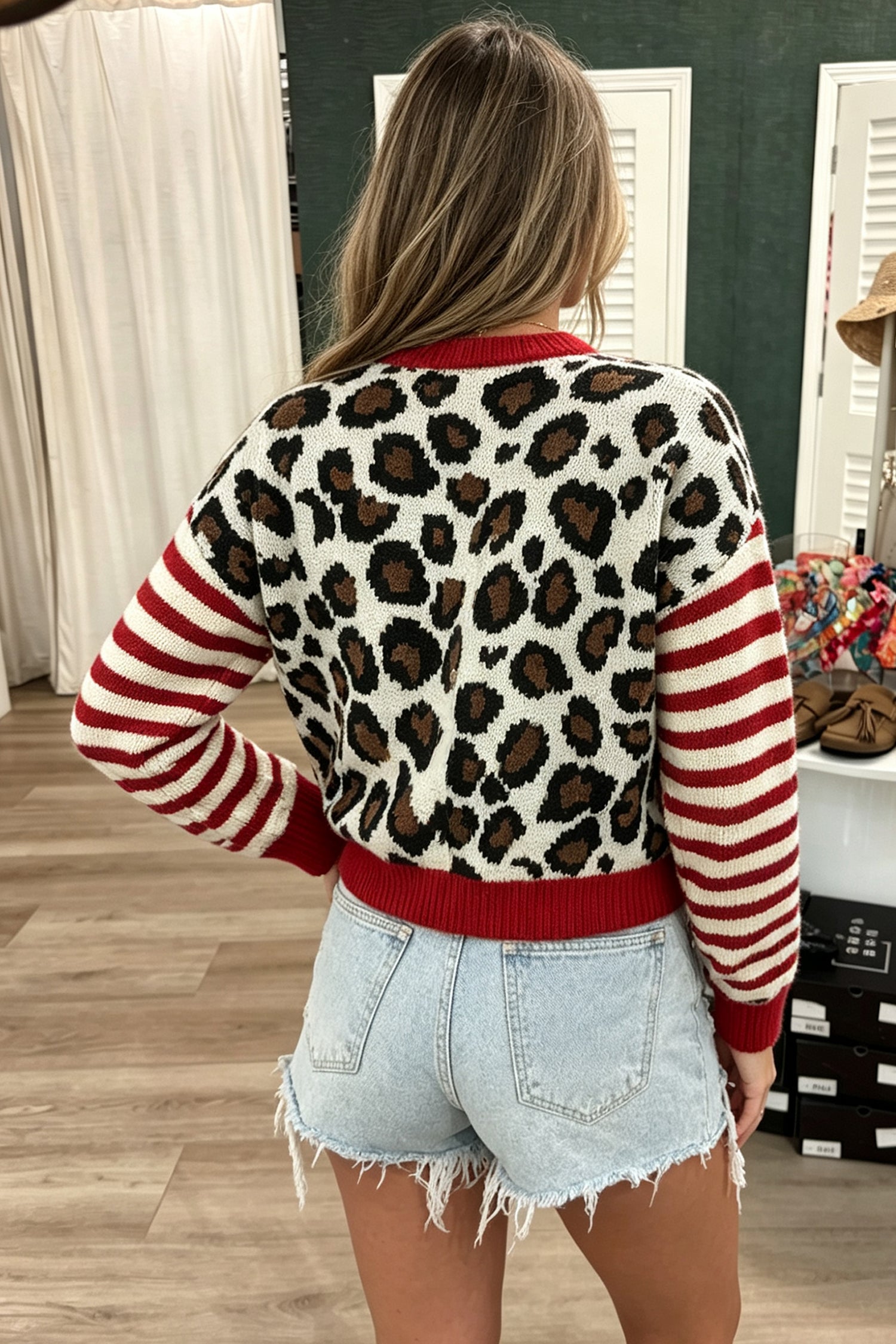 Back view of woman in leopard-print sweater with red-white striped sleeves and denim shorts.