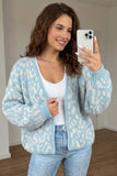 A woman takes a mirror selfie wearing a light blue and white patterned knit cardigan over a white tank top and light-wash blue jeans.