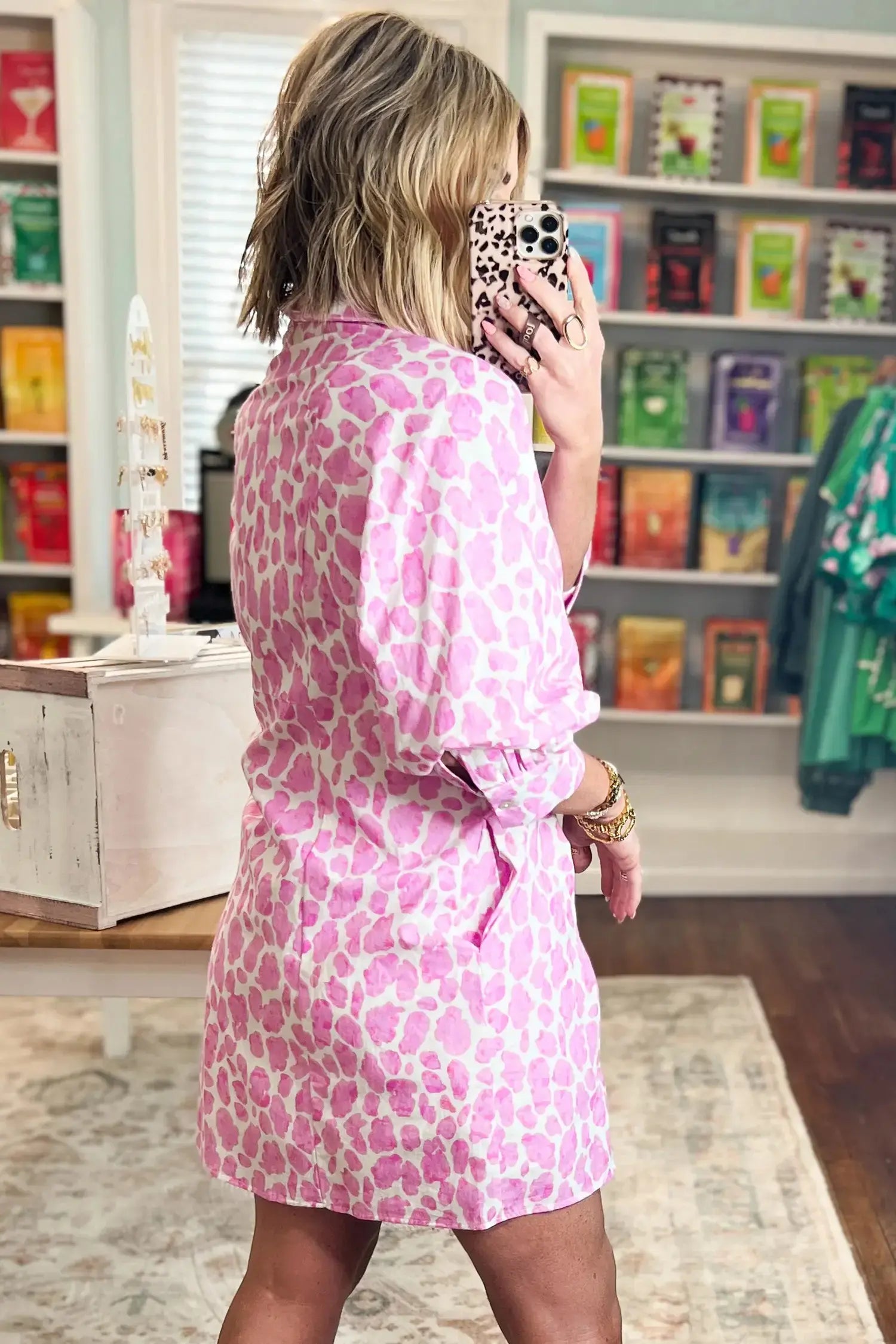 Woman in a pink leopard print dress talking on a phone in a store.