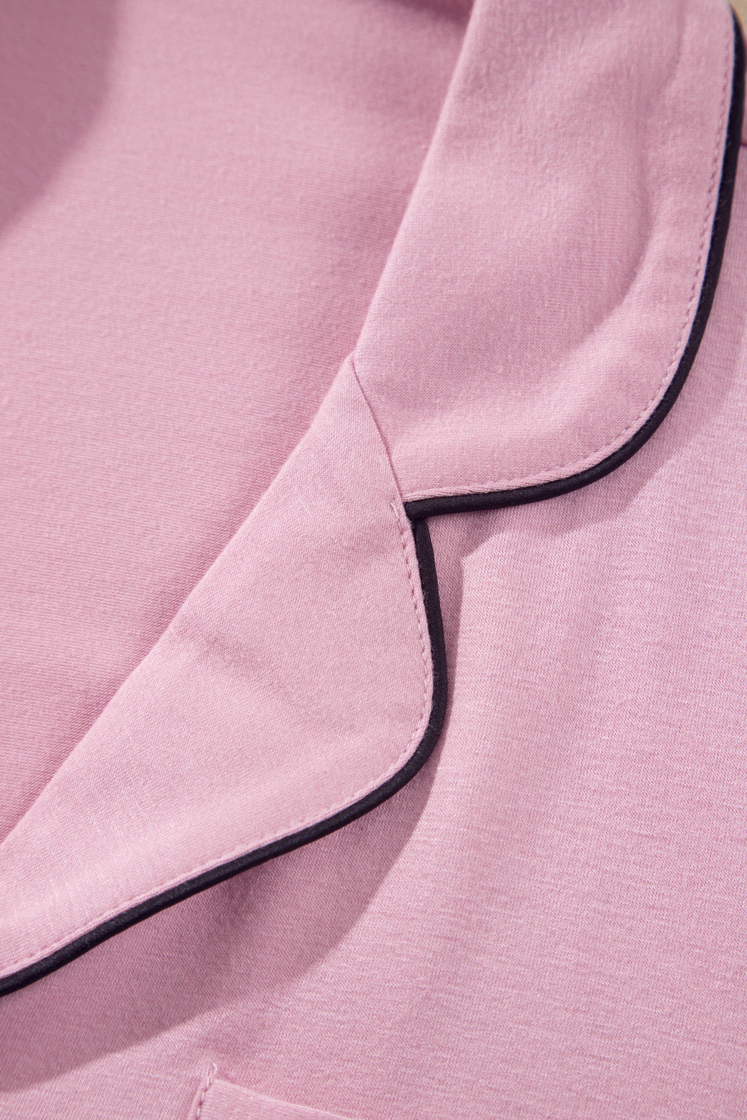 Close-up of a pink garment with black piping trim along the collar and pocket edges.
