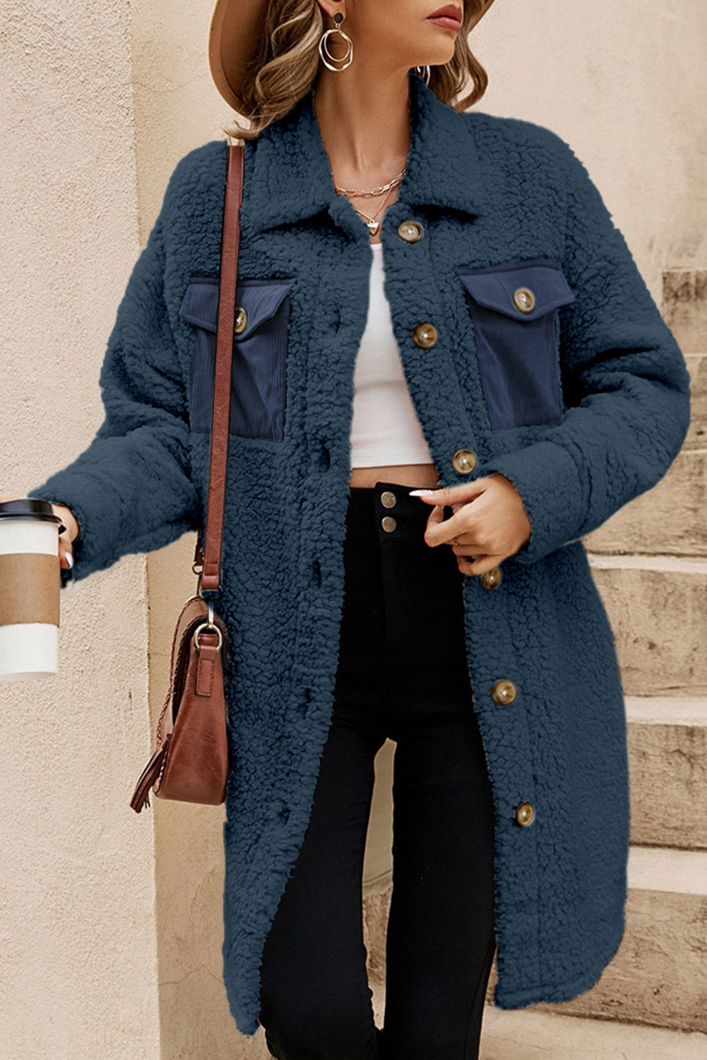 Woman wearing a blue coat with a brown handbag, standing on steps.