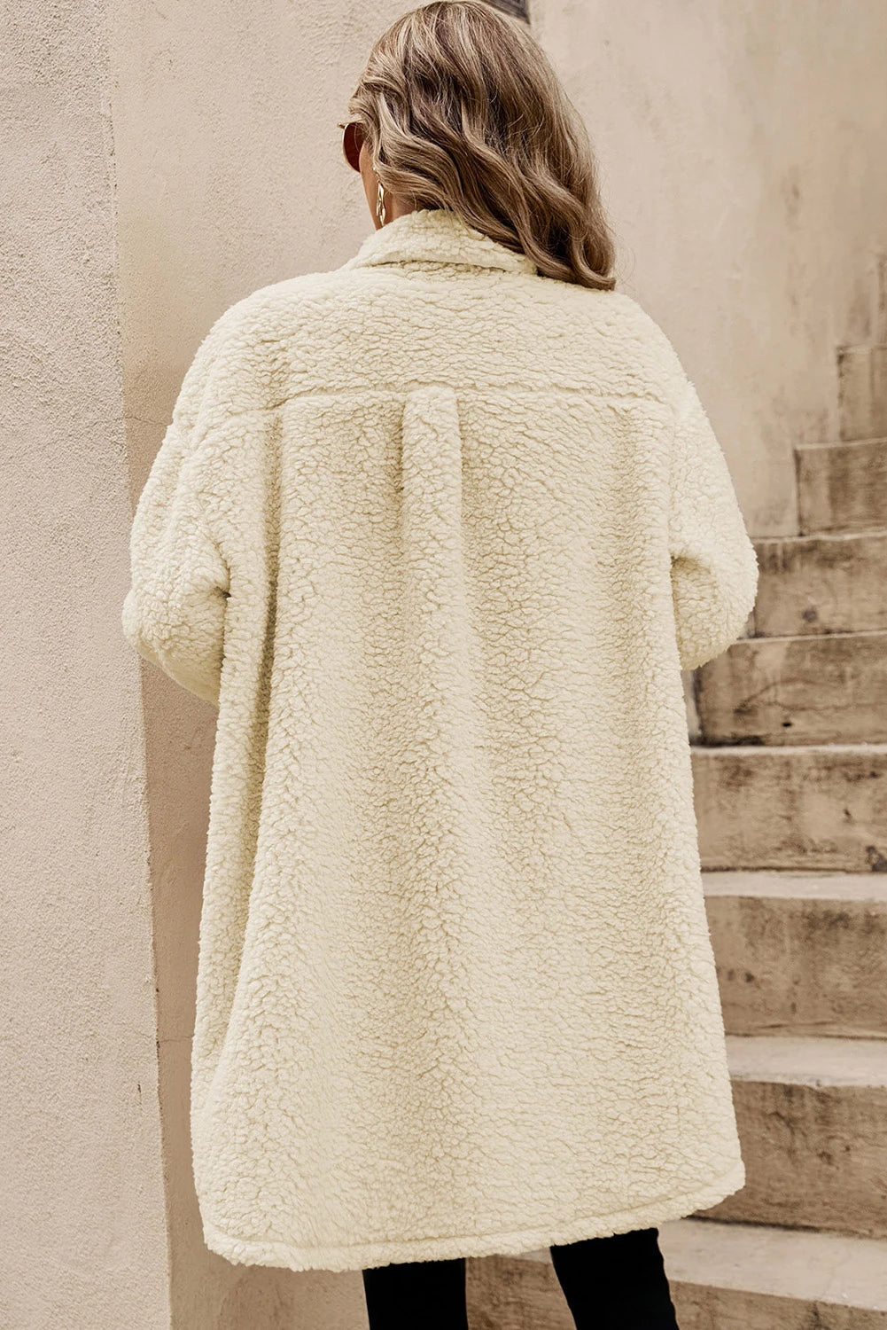 Person wearing a cream-colored sherpa coat standing on wooden steps.
