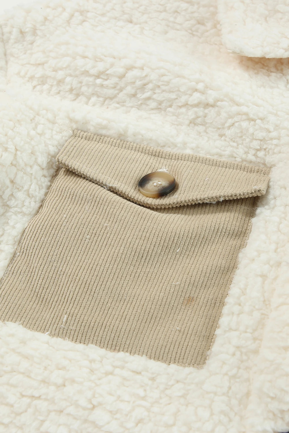 Close-up of a textured fabric with a pocket and button, featuring a neutral color palette.