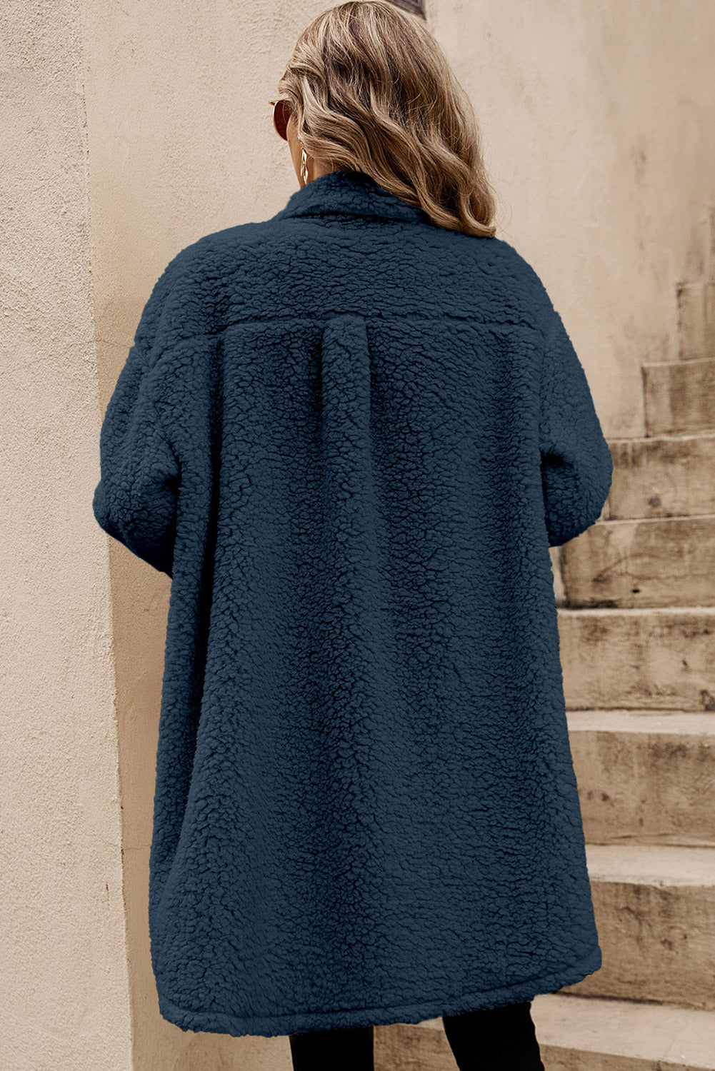 Person wearing a blue coat standing on stone steps.