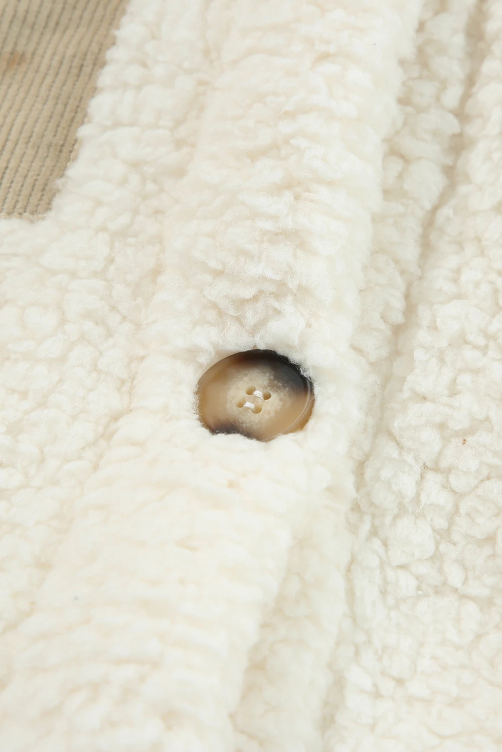 Close-up of cream sherpa fleece with brown button, soft texture, and beige woven lining.