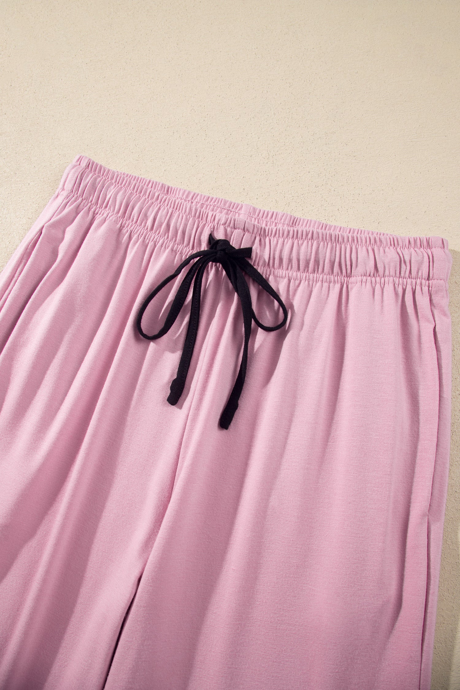Pink lounge pants with an elastic waistband and black drawstring, shown against a plain beige background.