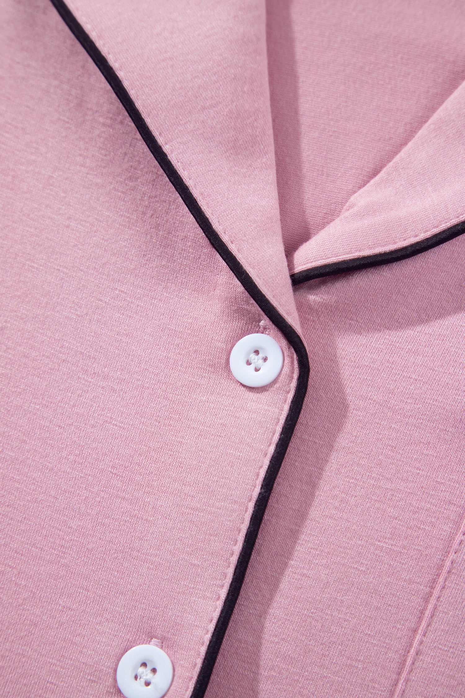 Close-up of a pink pajama shirt with black piping trim and white buttons.