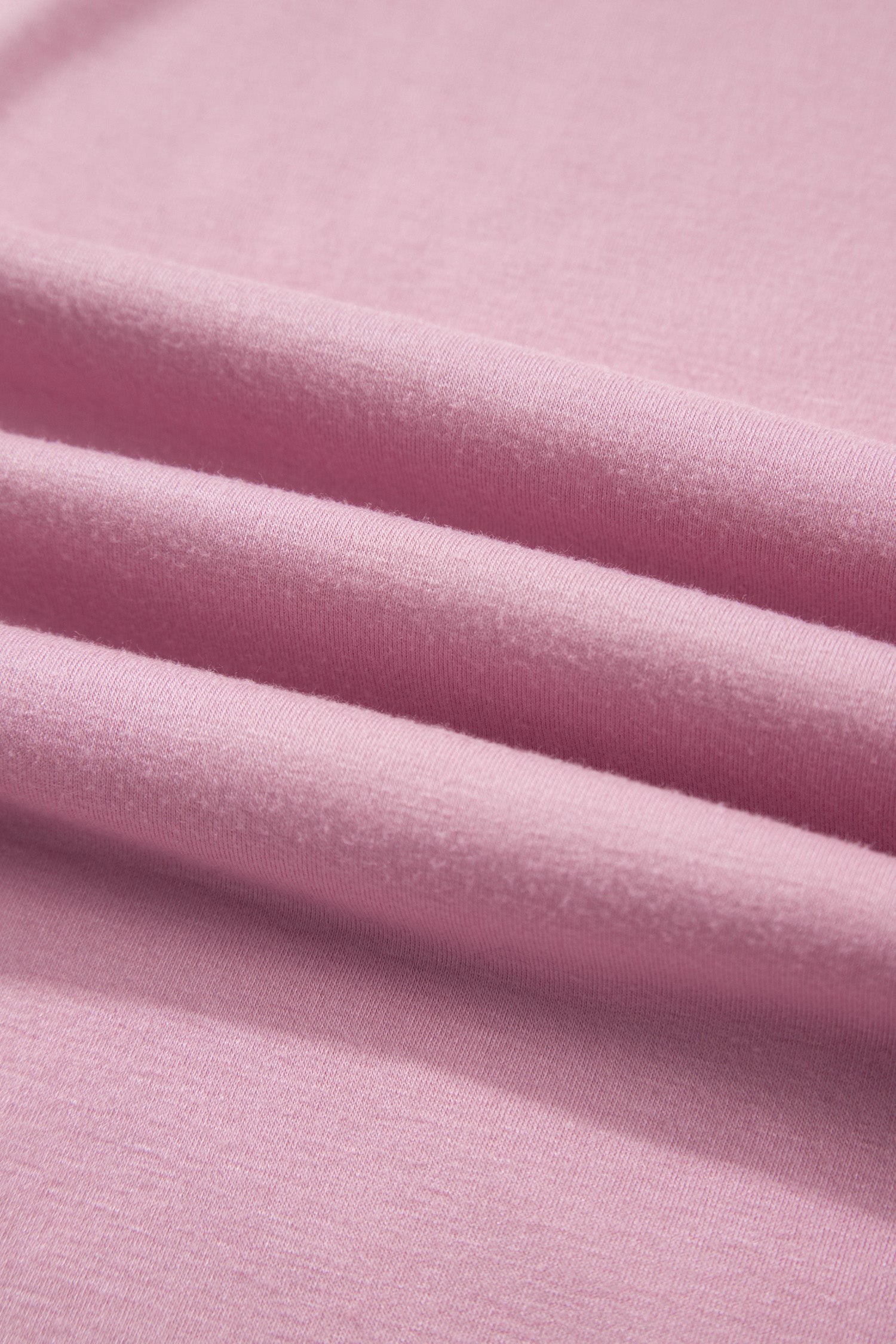 A close-up of soft pink fabric with gentle folds showing the material texture.