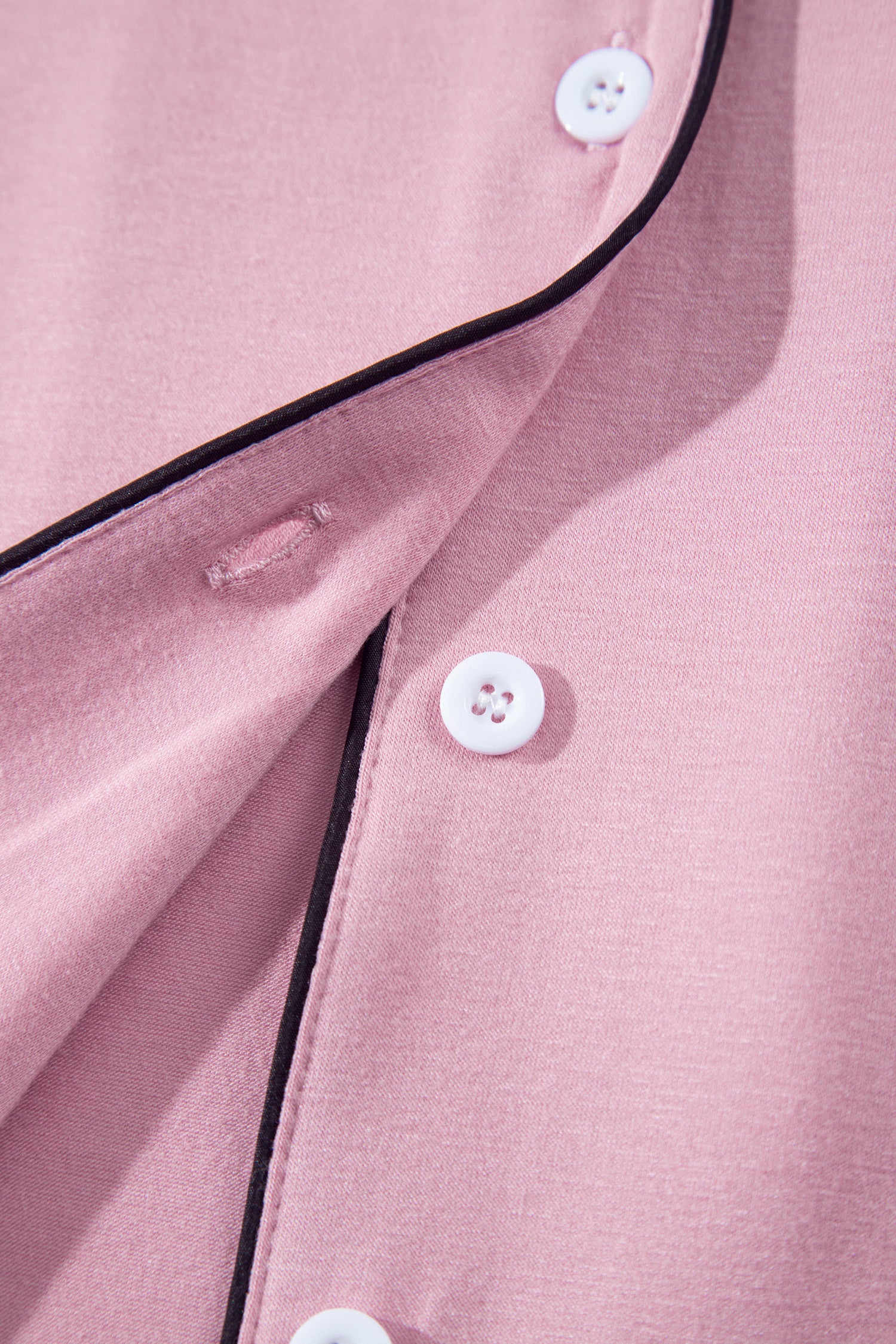 Close-up of a dusty pink button-up shirt with black piping trim and white buttons.