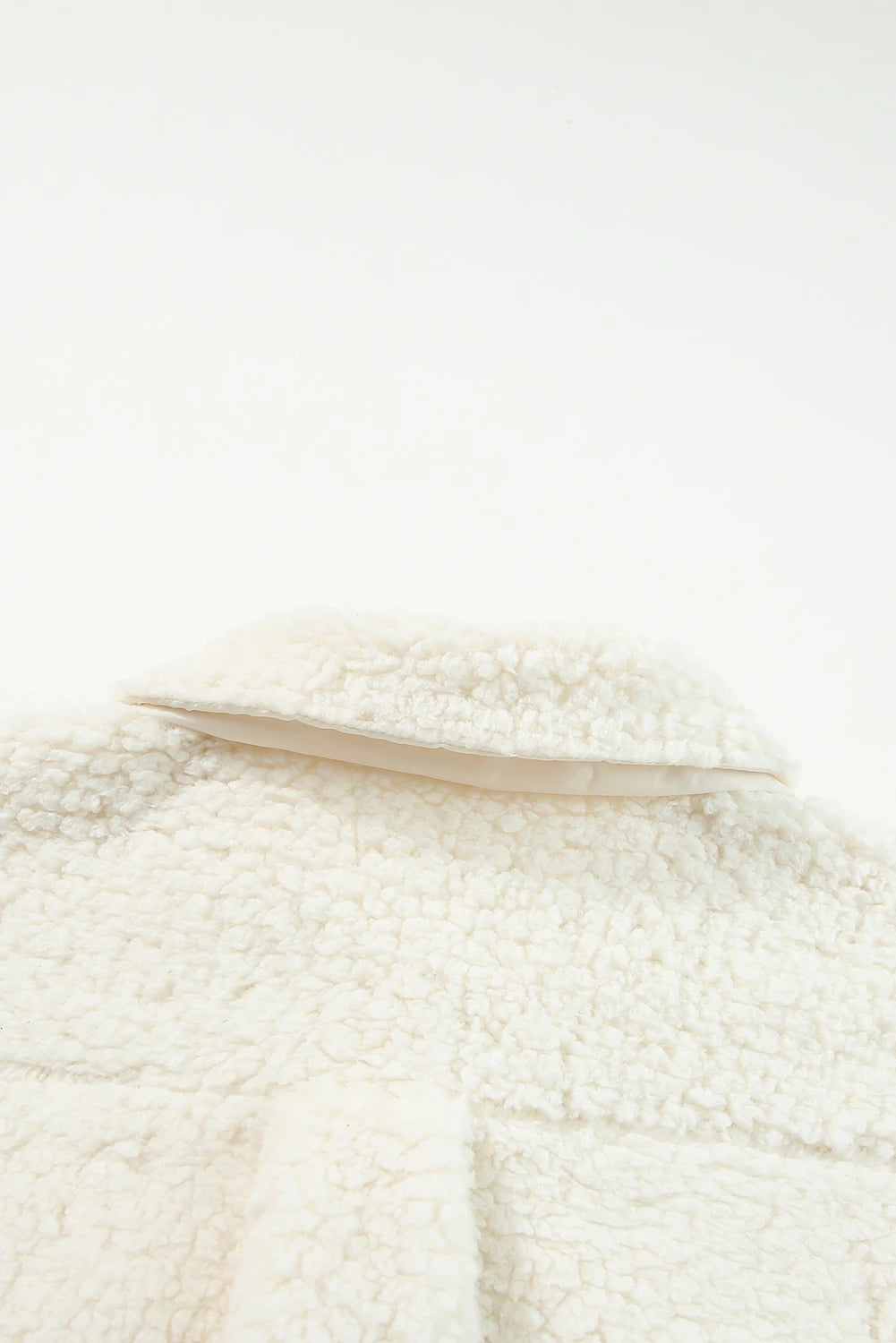 Close-up of cream sherpa fleece with soft texture and folded collar on white.