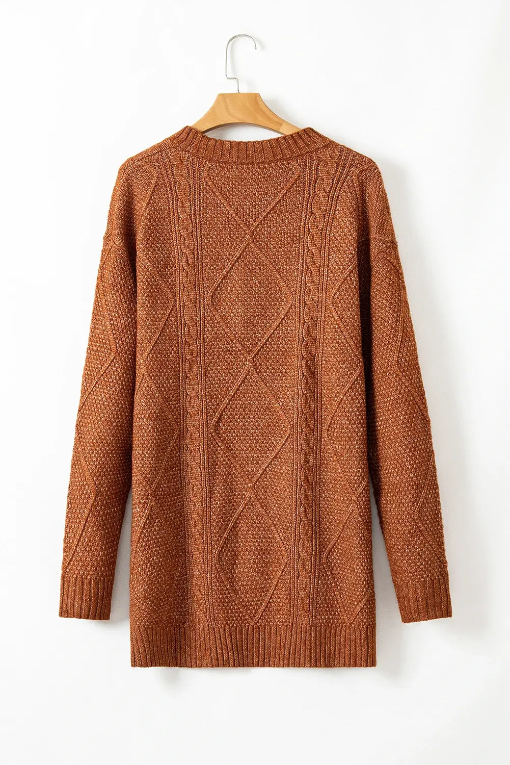 A rust-brown cable-knit sweater hanging on a wooden hanger against a plain white wall.