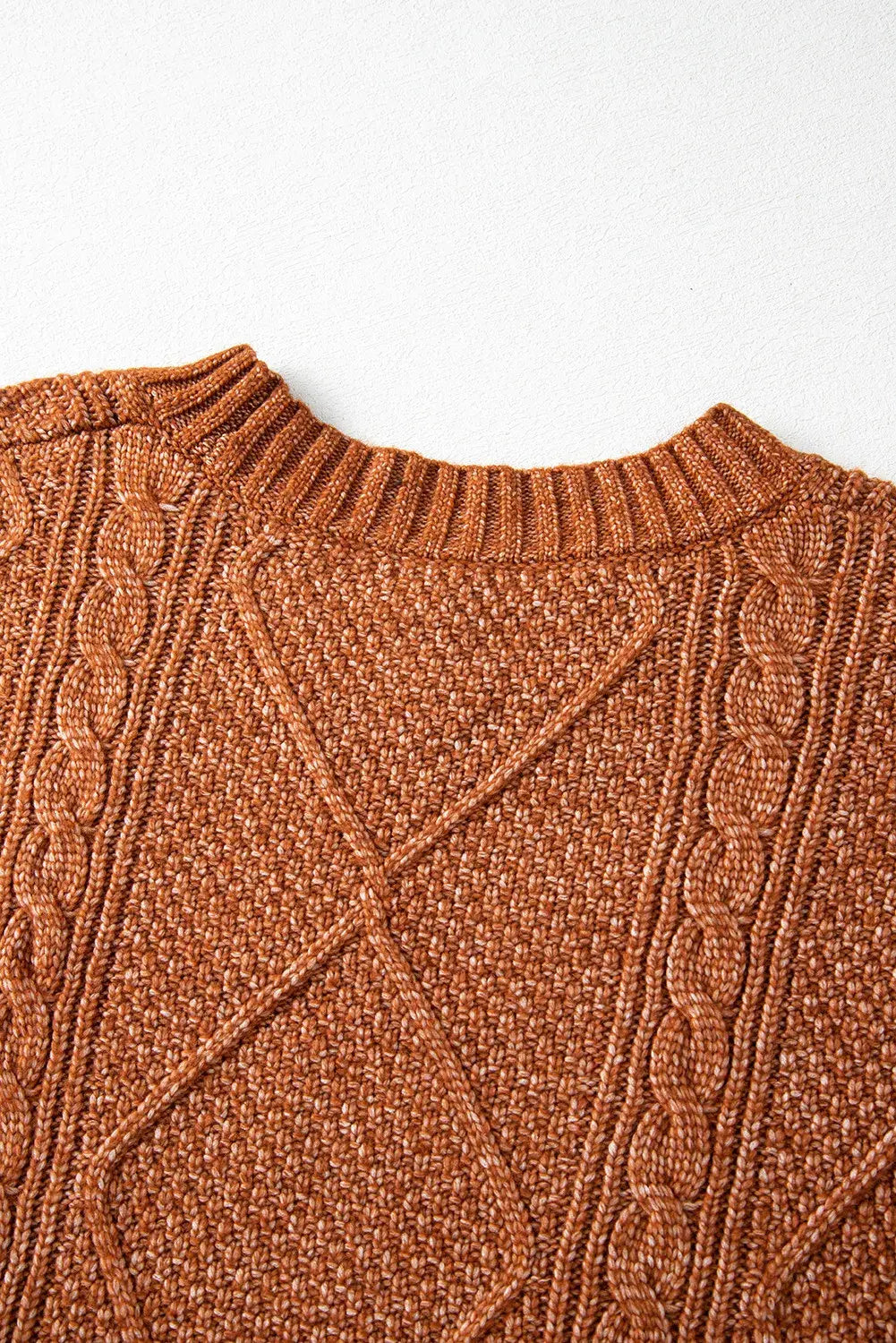 Close-up of a brown cable knit sweater on a light gray background