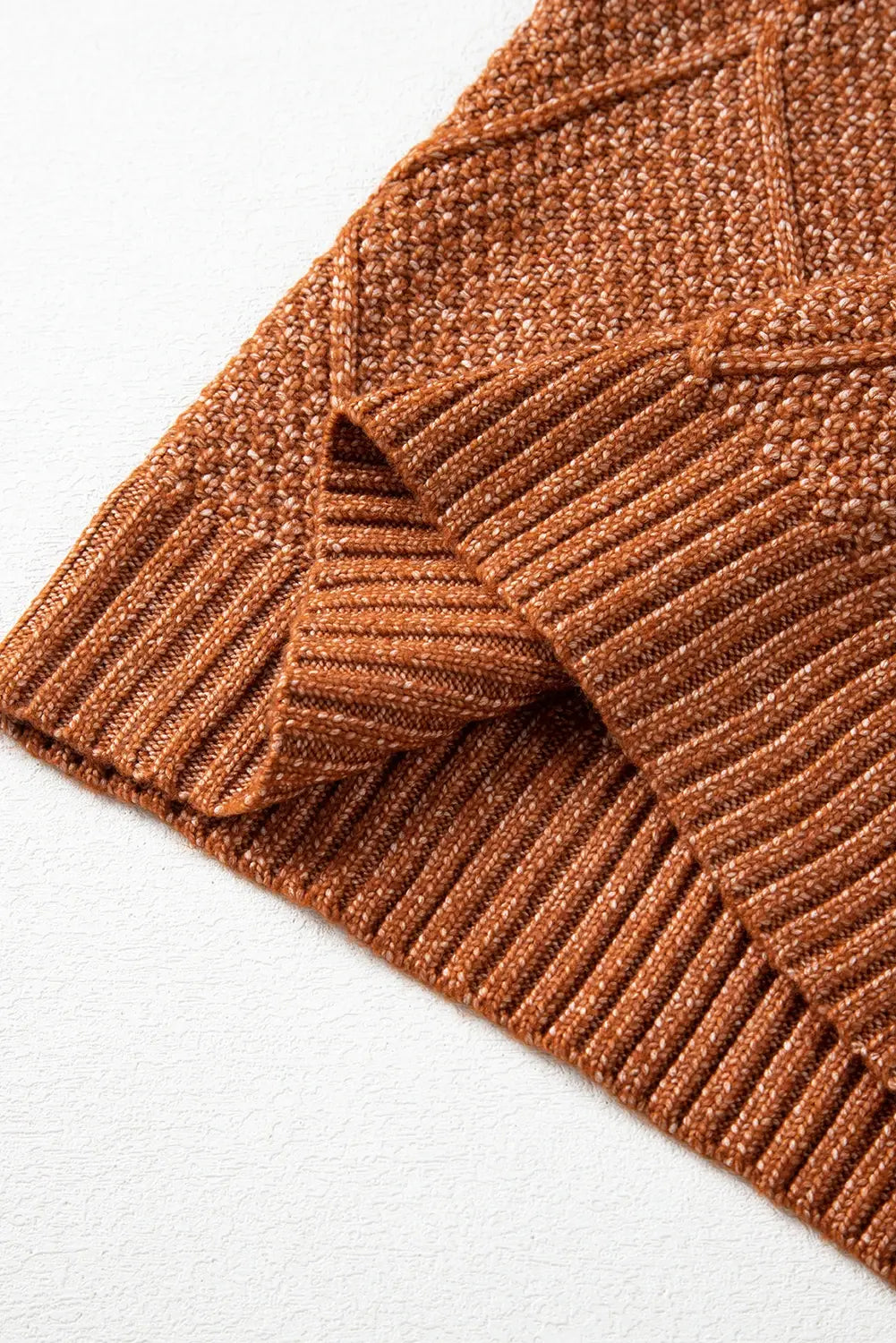 Close-up of a rust-brown knit sweater showing the ribbed cuff and textured knit pattern on a white background.