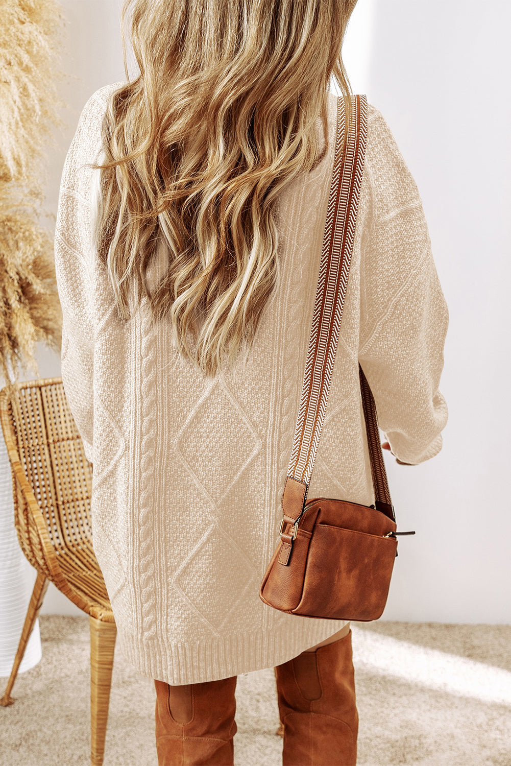 Person wearing a beige cable knit sweater and brown leather bag indoors.