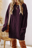 A woman wearing an oversized dark purple cable-knit sweater, styled with a brown crossbody bag and brown over-the-knee boots, standing next to a wicker chair.