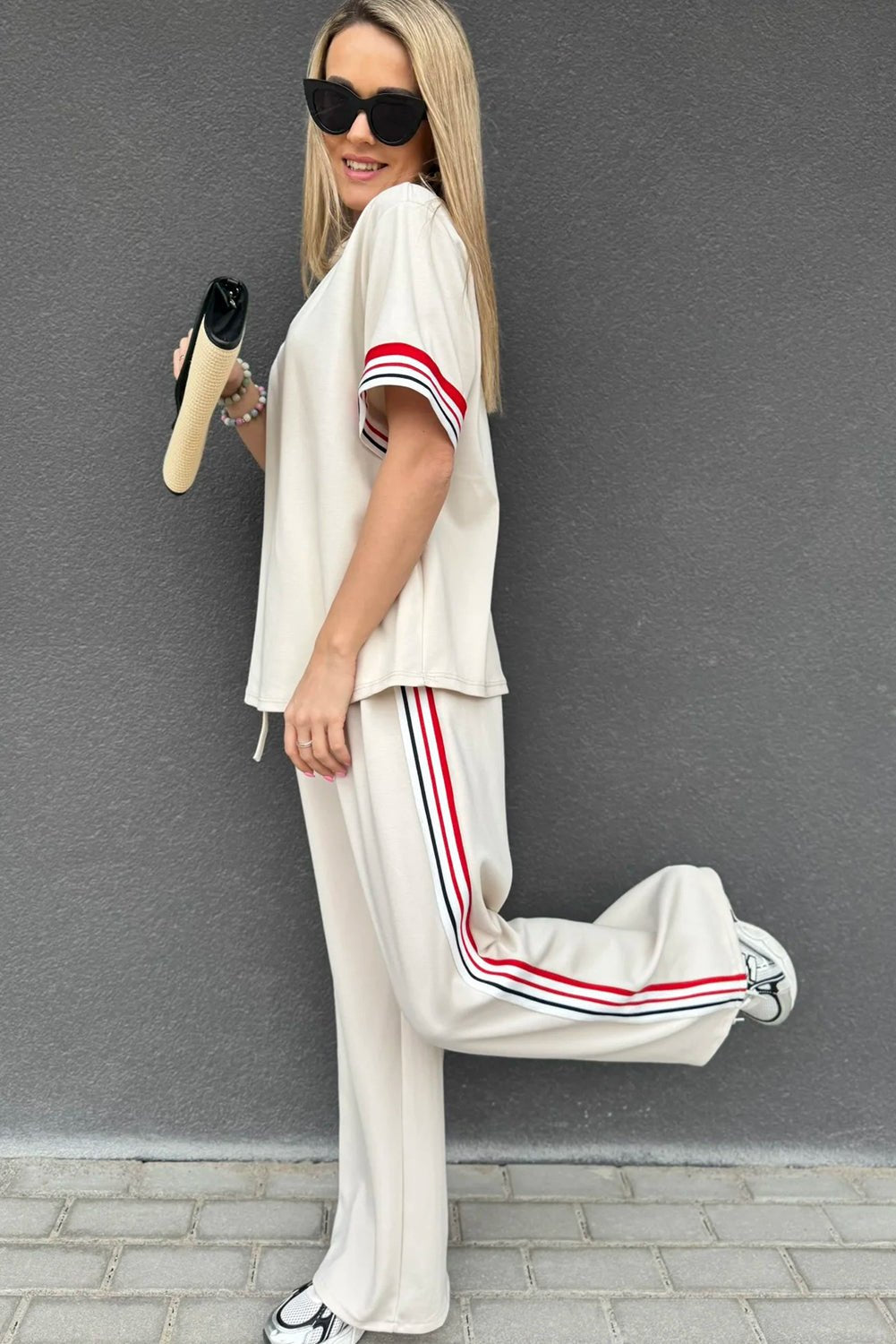 Woman wearing a white outfit with red and blue stripes against a gray wall.