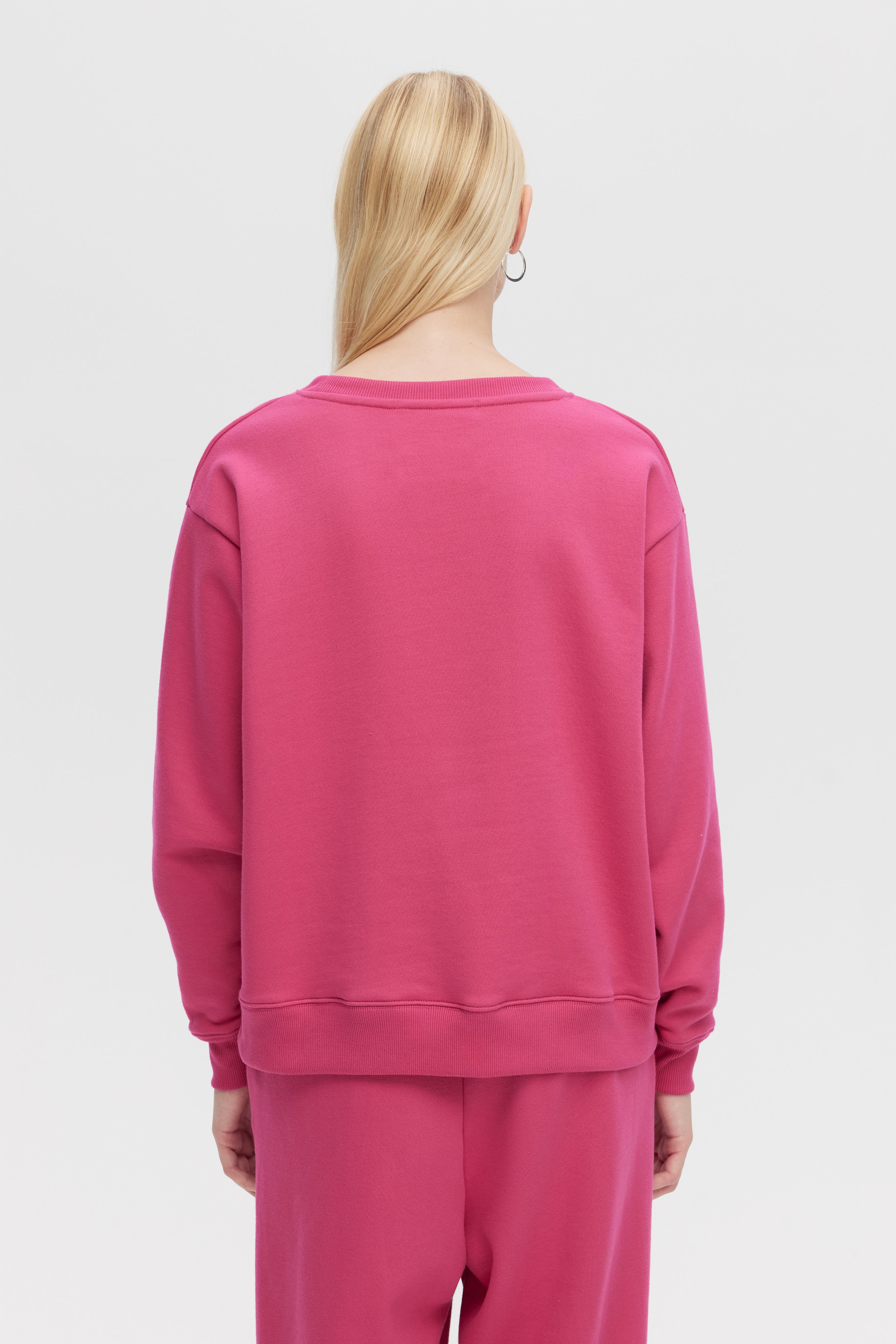 Person wearing a pink sweatshirt and pants on a white background