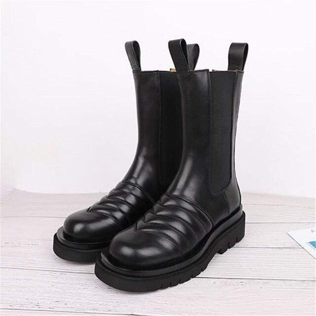 Pair of black leather boots with thick soles on a light wooden floor.