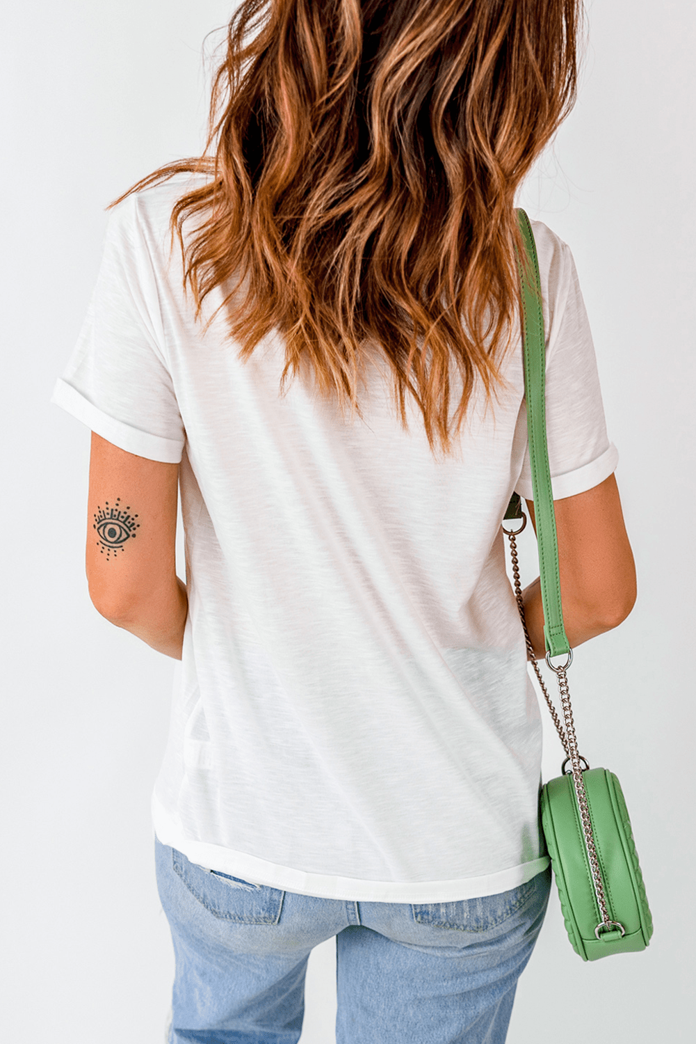 Person wearing a white t-shirt and blue jeans with a green handbag on a plain background