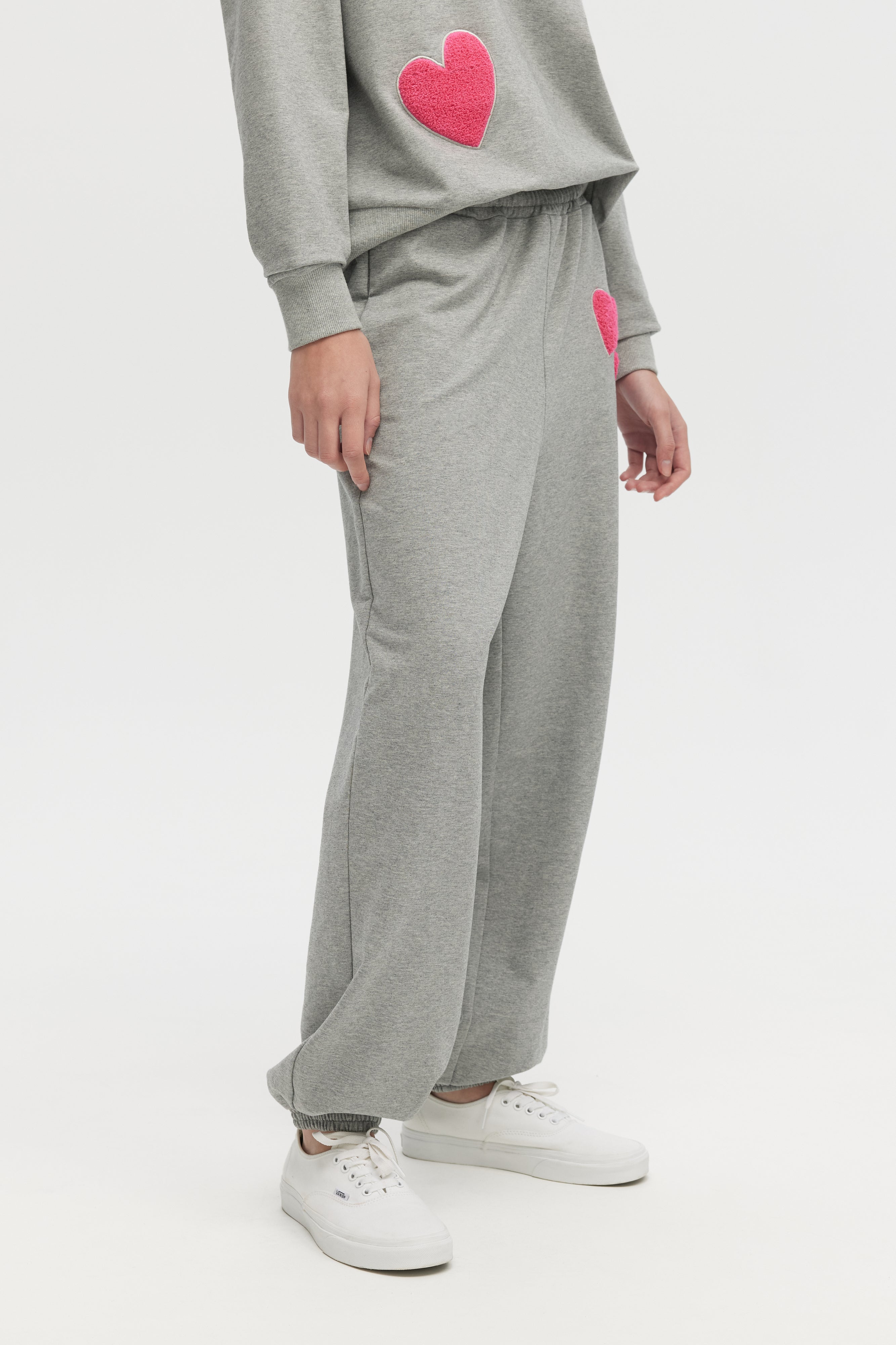Person wearing a gray sweatshirt and pants with pink heart designs on a white background