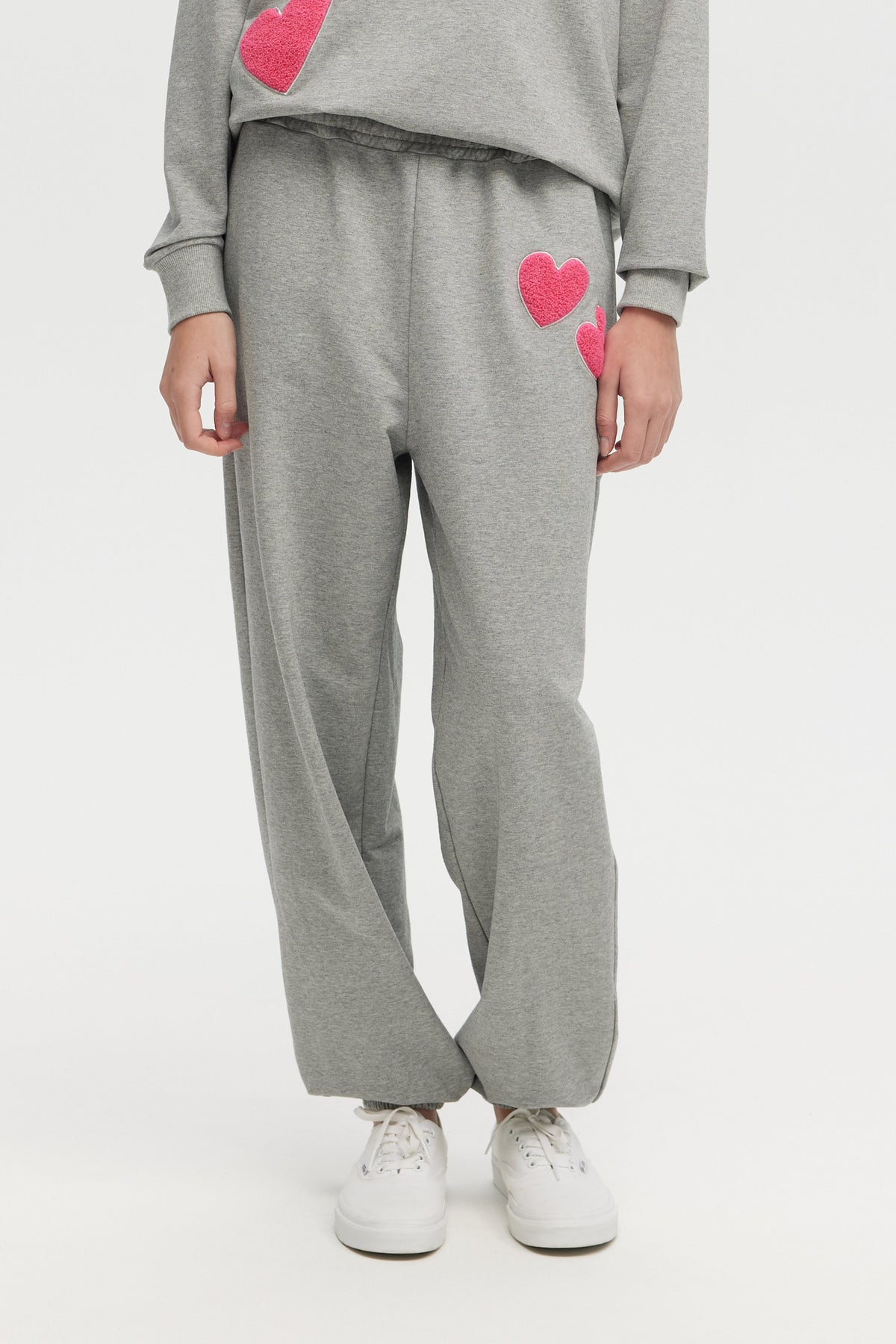 Person wearing gray sweatpants with pink hearts on a white background