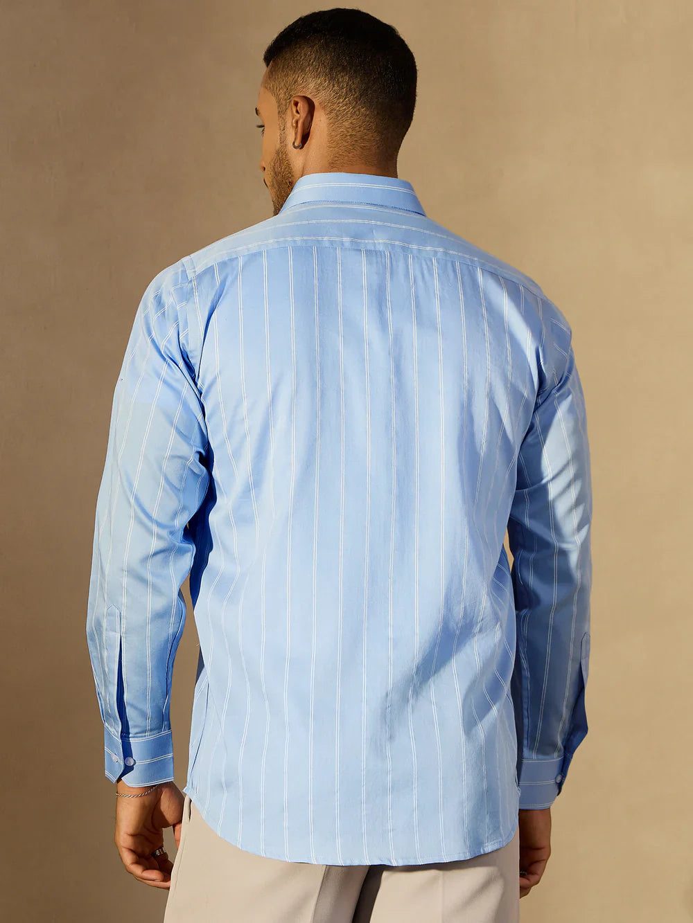 Man wearing a light blue striped shirt against a beige background