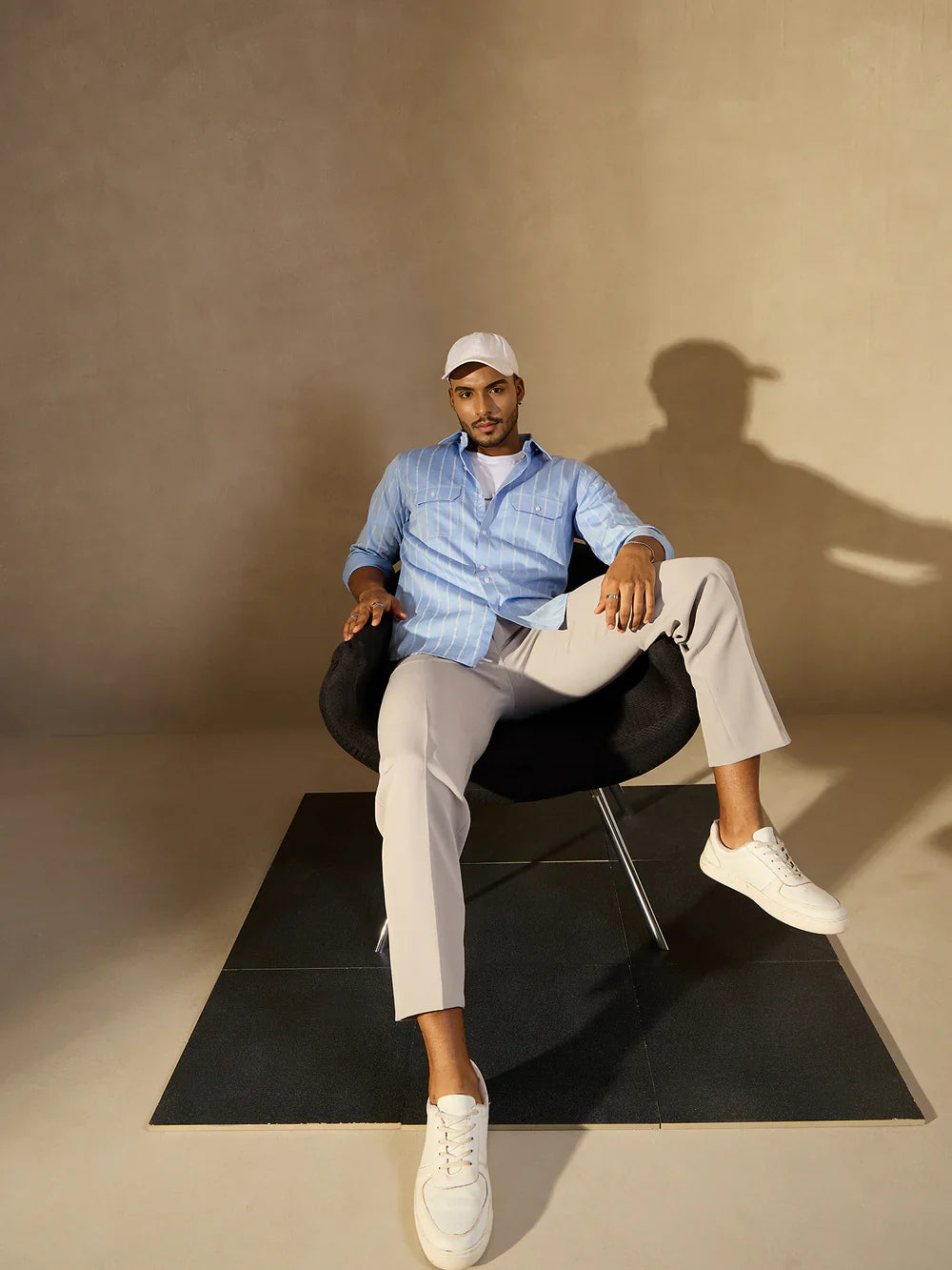 Man sitting on a black chair against a beige wall with a soft shadow.