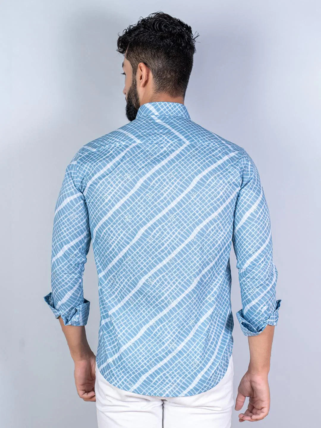 Man wearing a blue patterned shirt with rolled-up sleeves on a light gray background