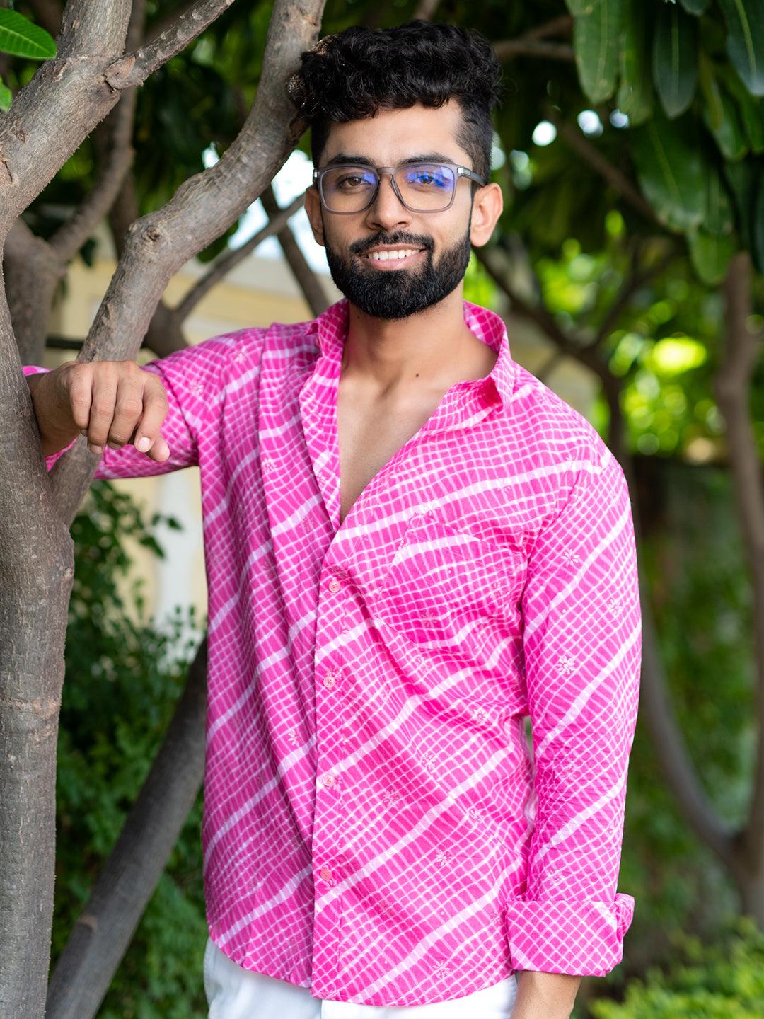 Man wearing a bright pink patterned shirt standing outdoors with greenery in the background