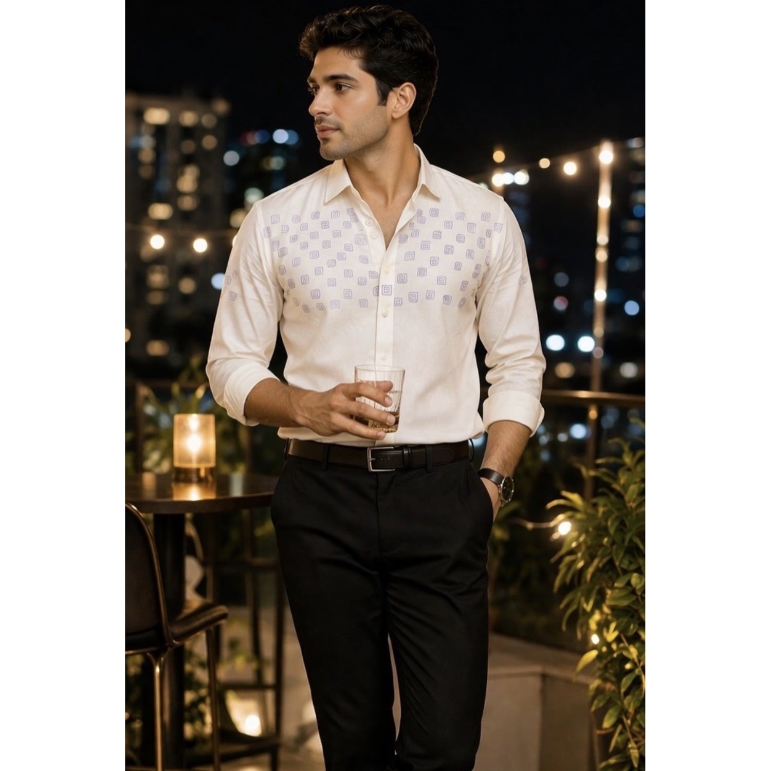 Man in a white shirt and black pants holding a drink on a rooftop at night.