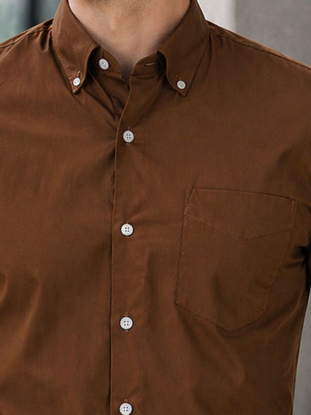 Close-up of a brown button-up shirt with a pocket on a neutral background