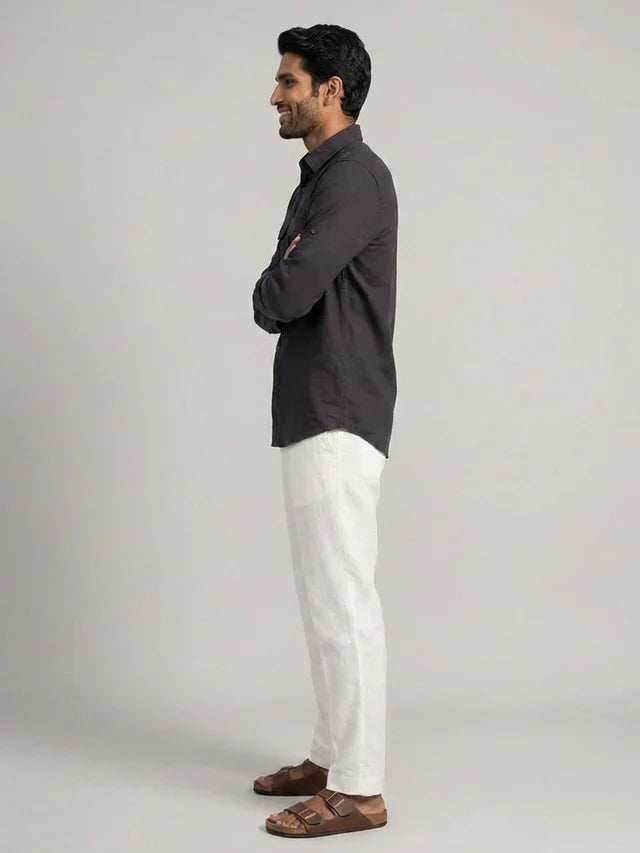 Man wearing a dark shirt and white pants standing against a plain background
