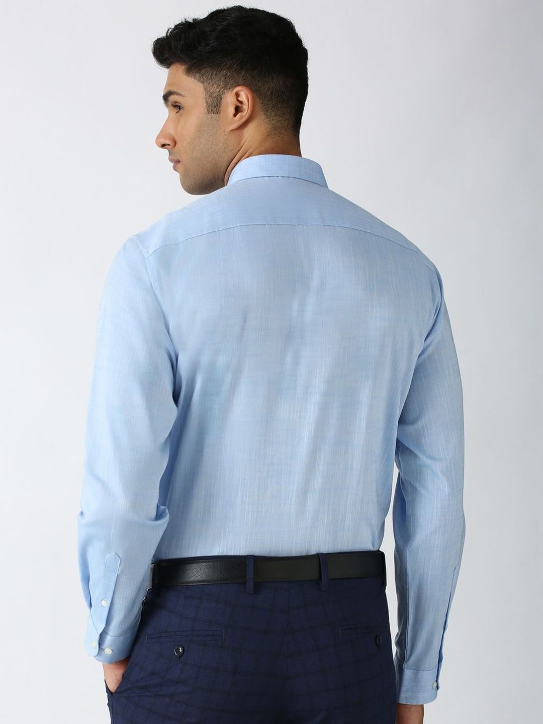 Man wearing a light blue dress shirt and dark pants on a white background