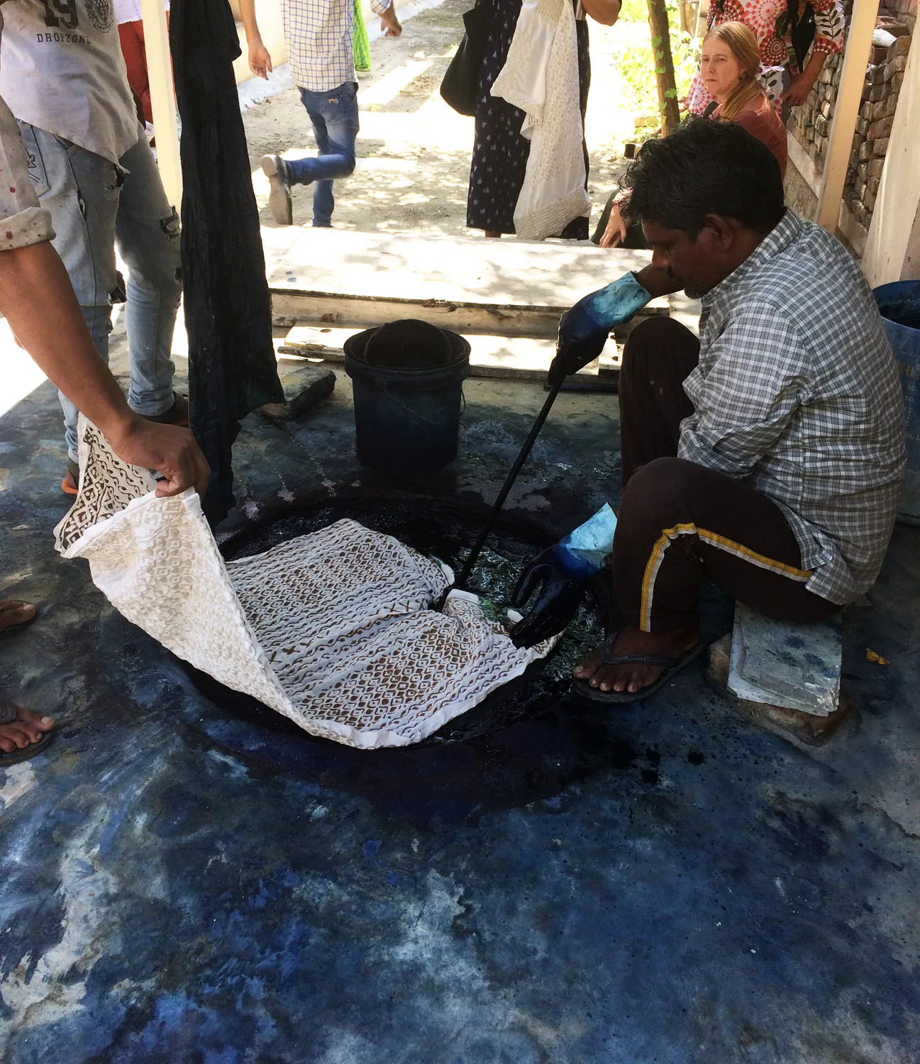 Person dyeing fabric with a bucket and dye brush on a blue surface.