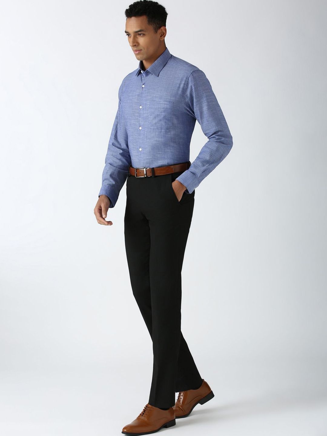 Man wearing a blue checkered shirt, black pants, and brown shoes on a white background