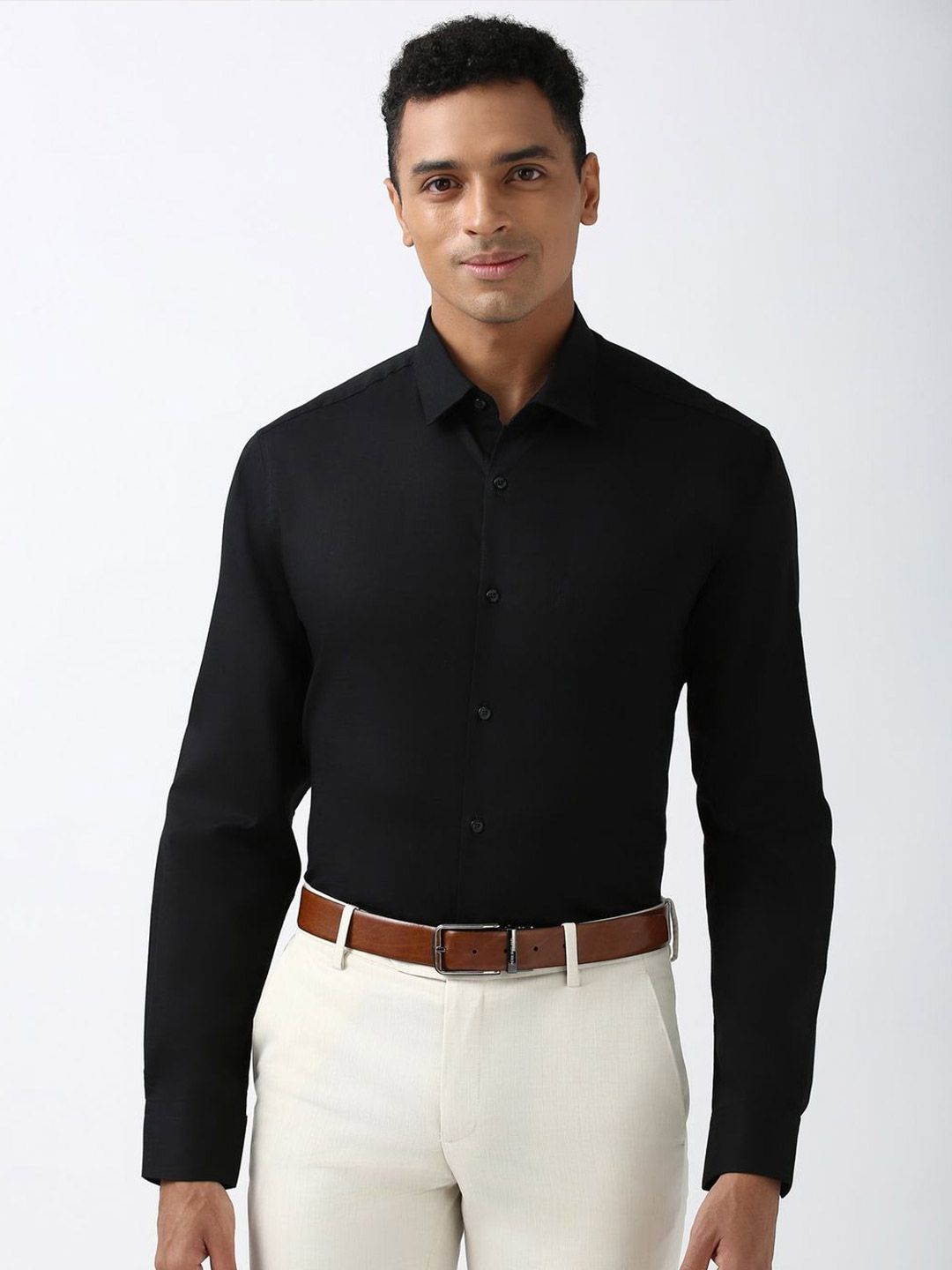 Man wearing a black dress shirt and white pants with a brown belt on a white background
