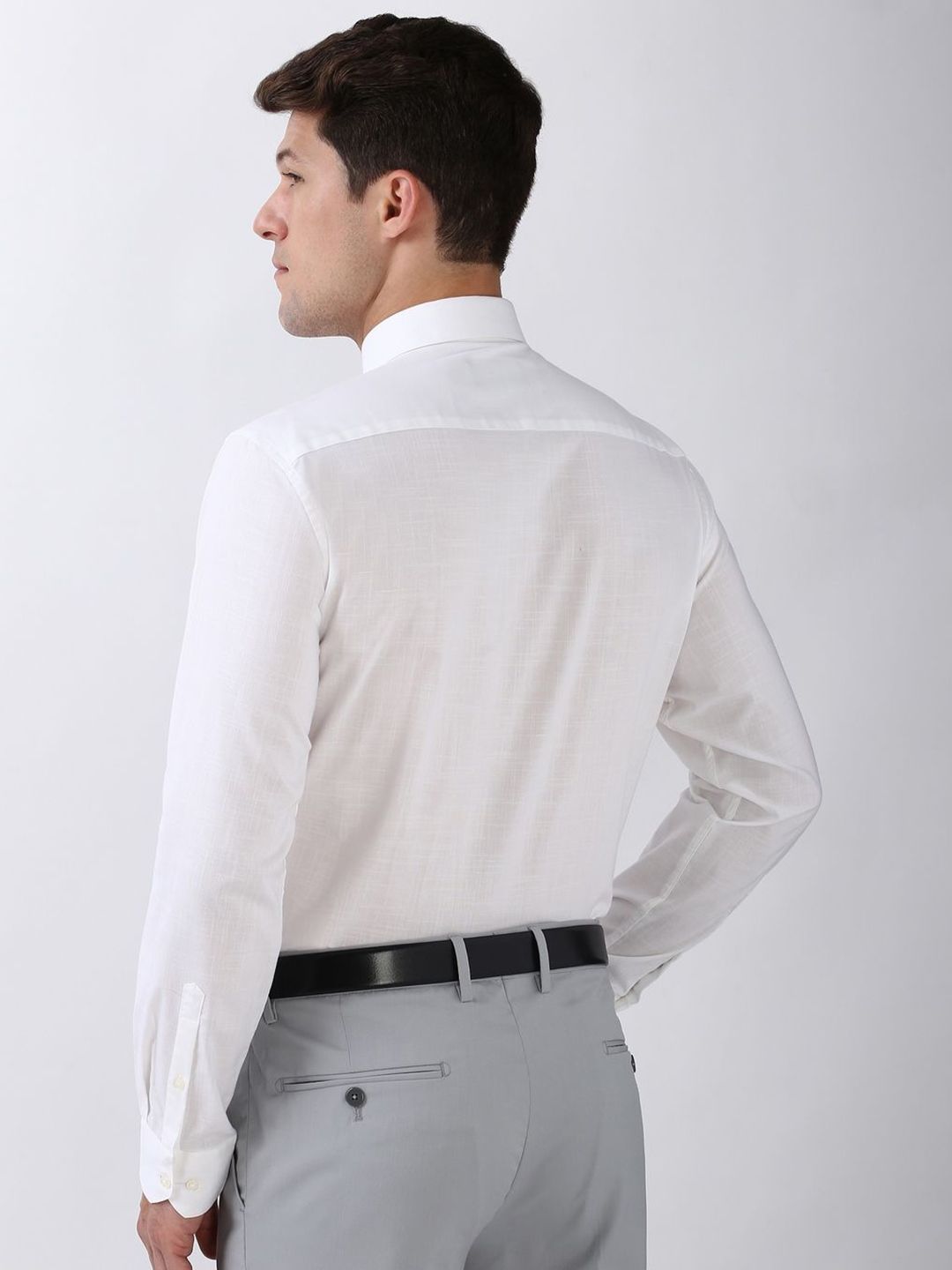 Man wearing a white dress shirt and gray pants on a plain background