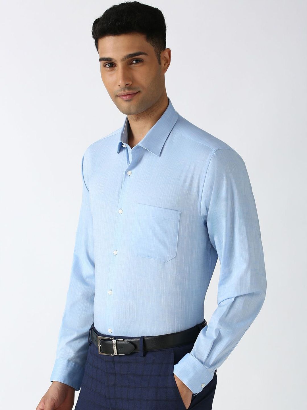 Man wearing a light blue dress shirt and dark pants on a white background