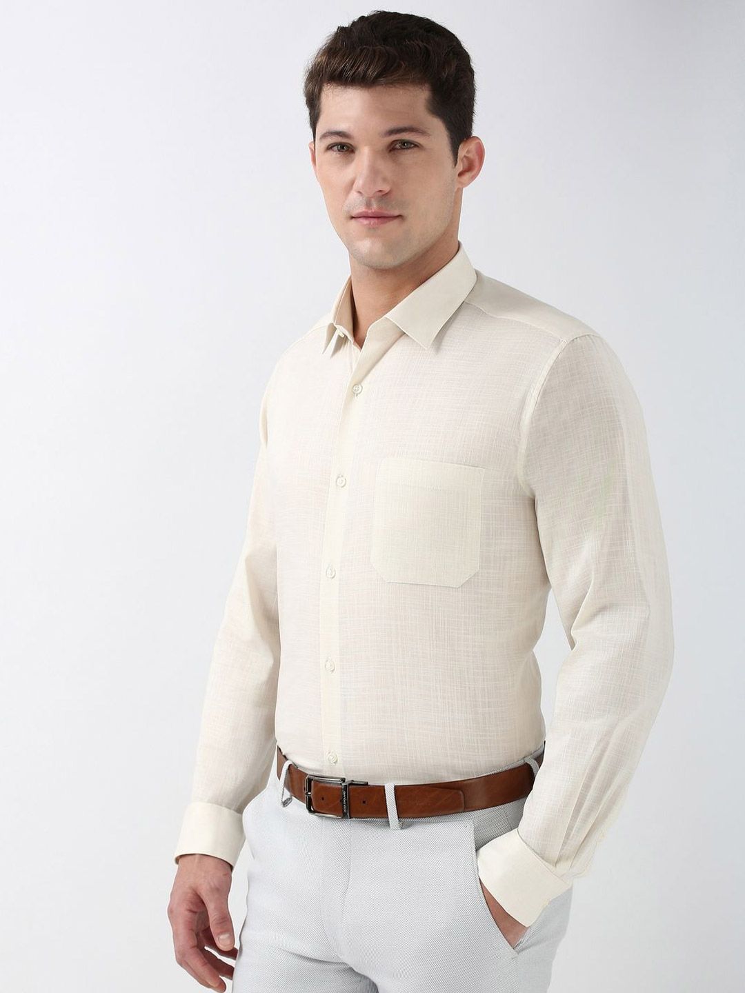 Man wearing a beige button-up shirt and white pants on a plain background