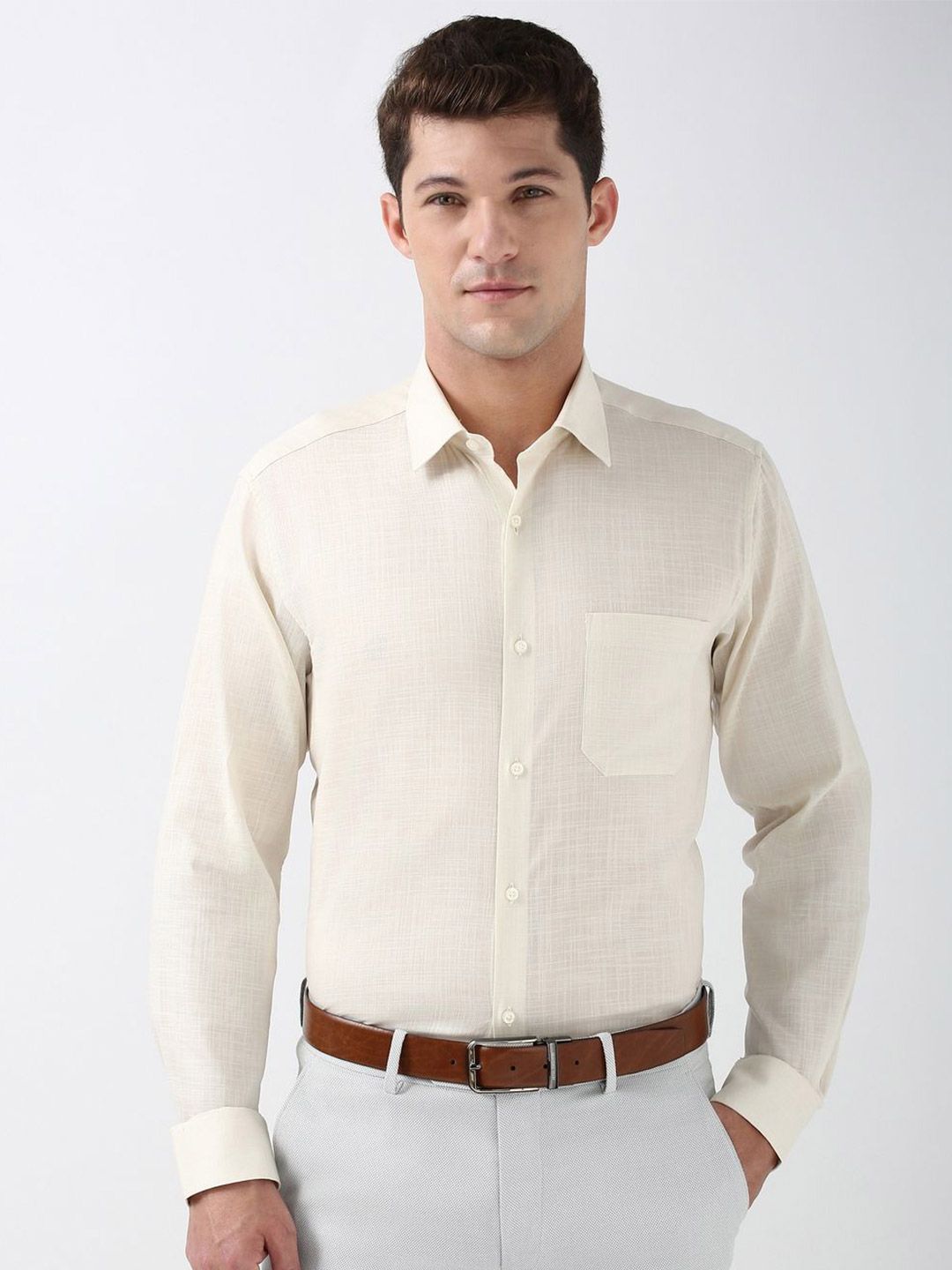 Man wearing a beige dress shirt with a brown belt on a white background
