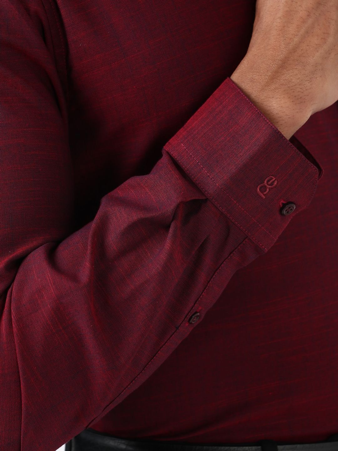 Close-up of a maroon shirt with rolled-up sleeve and button details.