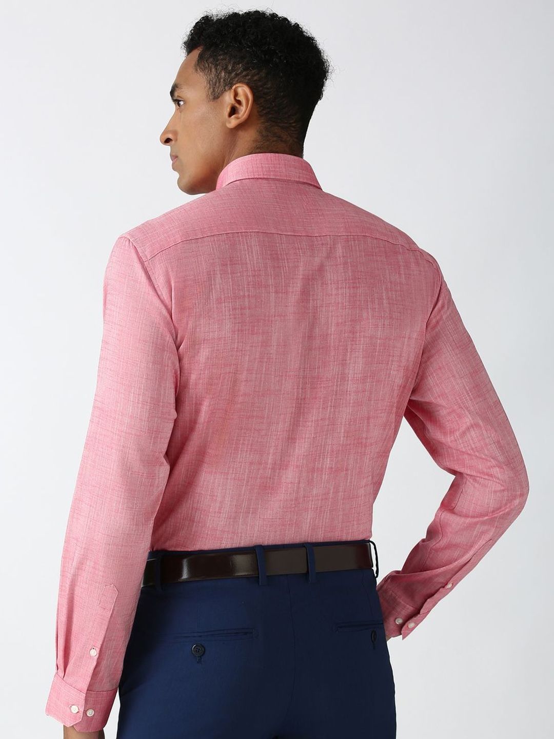 Man wearing a pink checkered shirt and dark pants on a white background