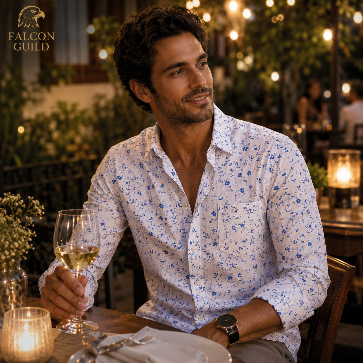 Man sitting at a table with a glass of wine in a restaurant setting, wearing a floral shirt.