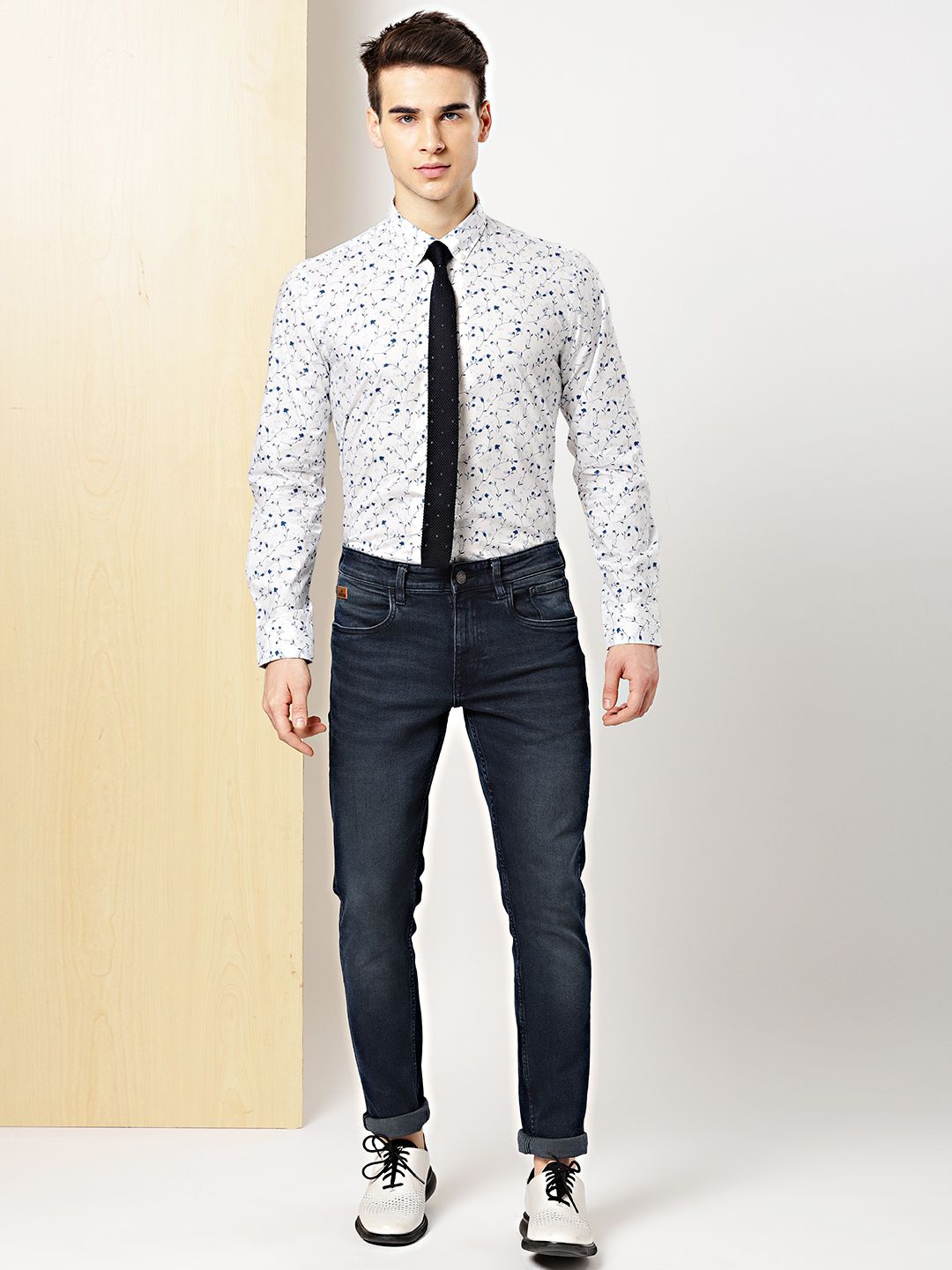 Man wearing a patterned shirt and dark jeans against a plain background