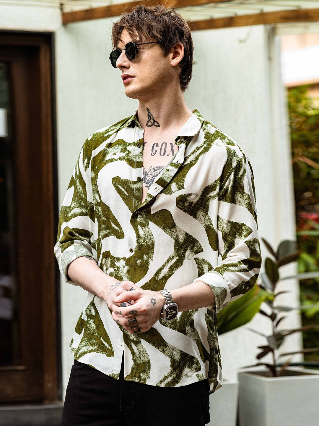 Person wearing a green and white patterned shirt with tattoos outdoors.